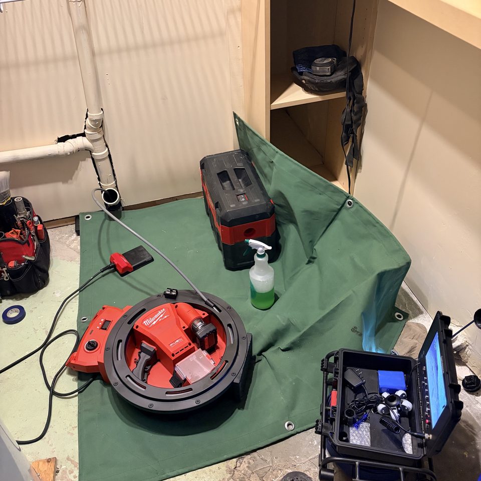 Drain auger, sewer camera and shop vac set up on a drop cloth at a basement cleanout